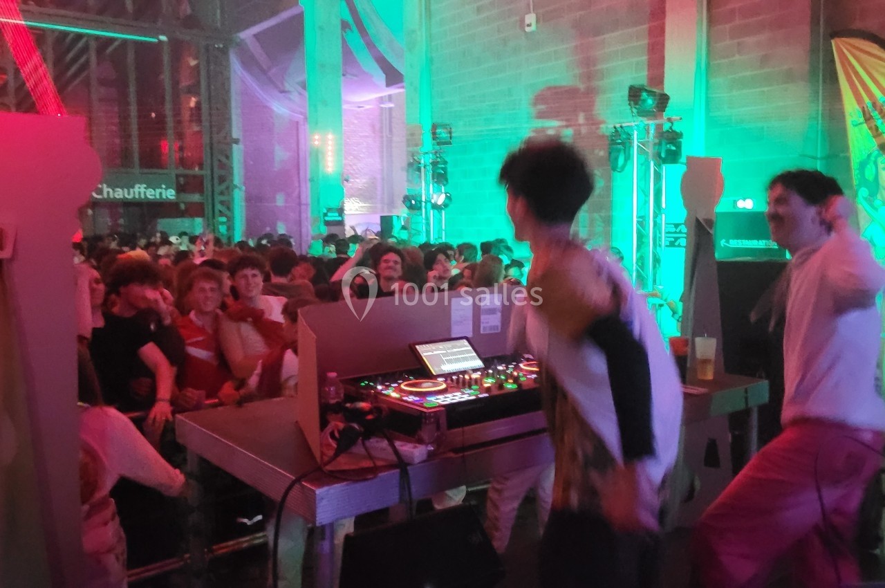 Des DJ animent une soirée festive dans une salle éclairée de lumières colorées, avec un public dansant.