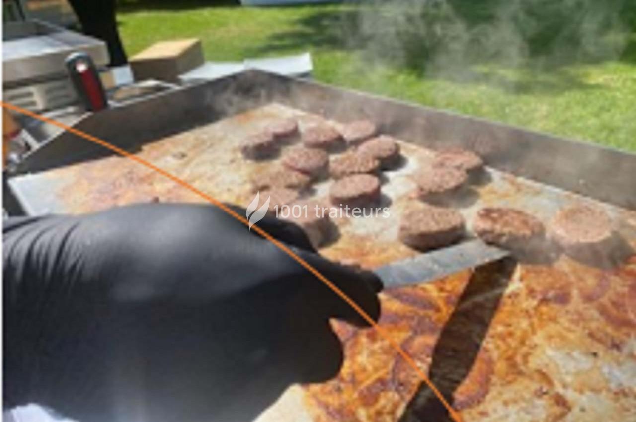 Cuisson de plusieurs steaks hachés sur une plaque chauffante, une main gantée tenant une spatule.