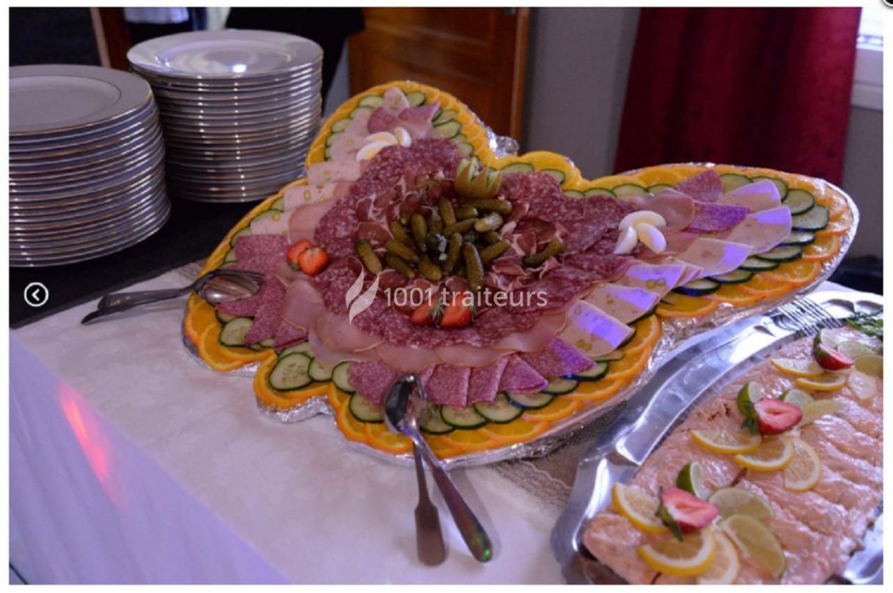 Plateau de charcuterie en forme de papillon, décoré de légumes, cornichons et fraises, avec assiettes empilées à côté.