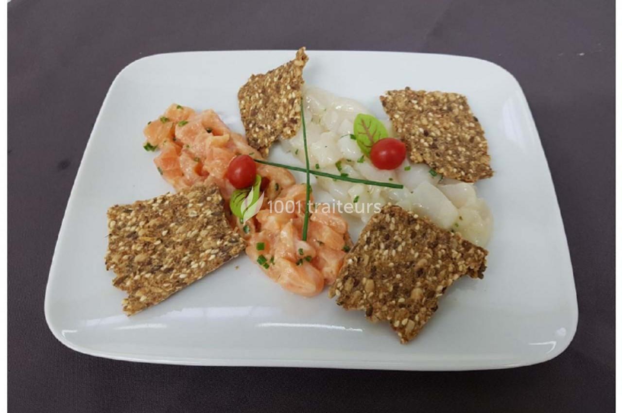 Assiette composée de tartare de saumon, de carpaccio de Saint-Jacques, de crackers aux graines et de décorations végétales.