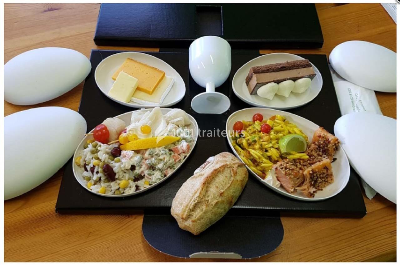 Plateau-repas avec pain, fromage, salade composée, poisson, desserts variés et verre sur une table en bois.