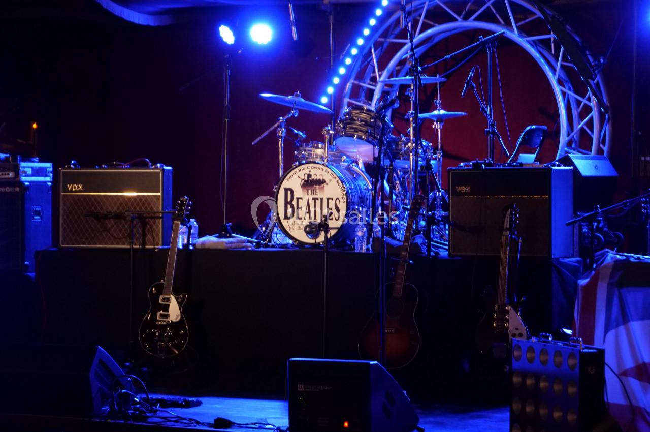 Scène de concert avec instruments de musique, amplificateurs et une batterie portant le logo des Beatles.