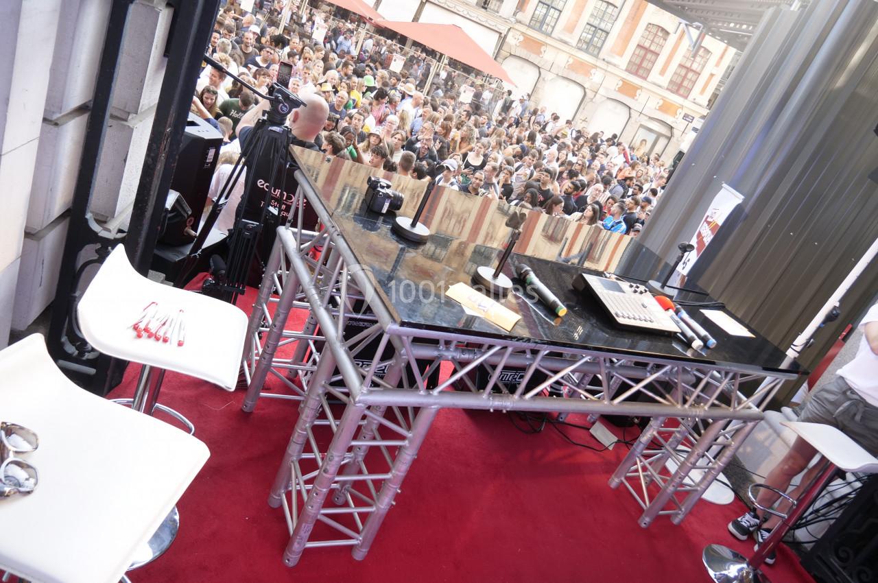 Vue d'une scène avec une table de mixage et des équipements audio, face à une foule rassemblée en extérieur.