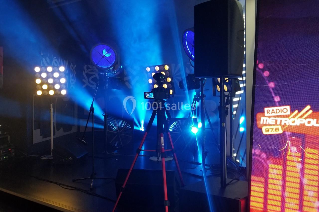 Scène avec éclairage bleu, projecteurs, trépied avec caméra et écran affichant ’Radio Metropolys 97.6’.