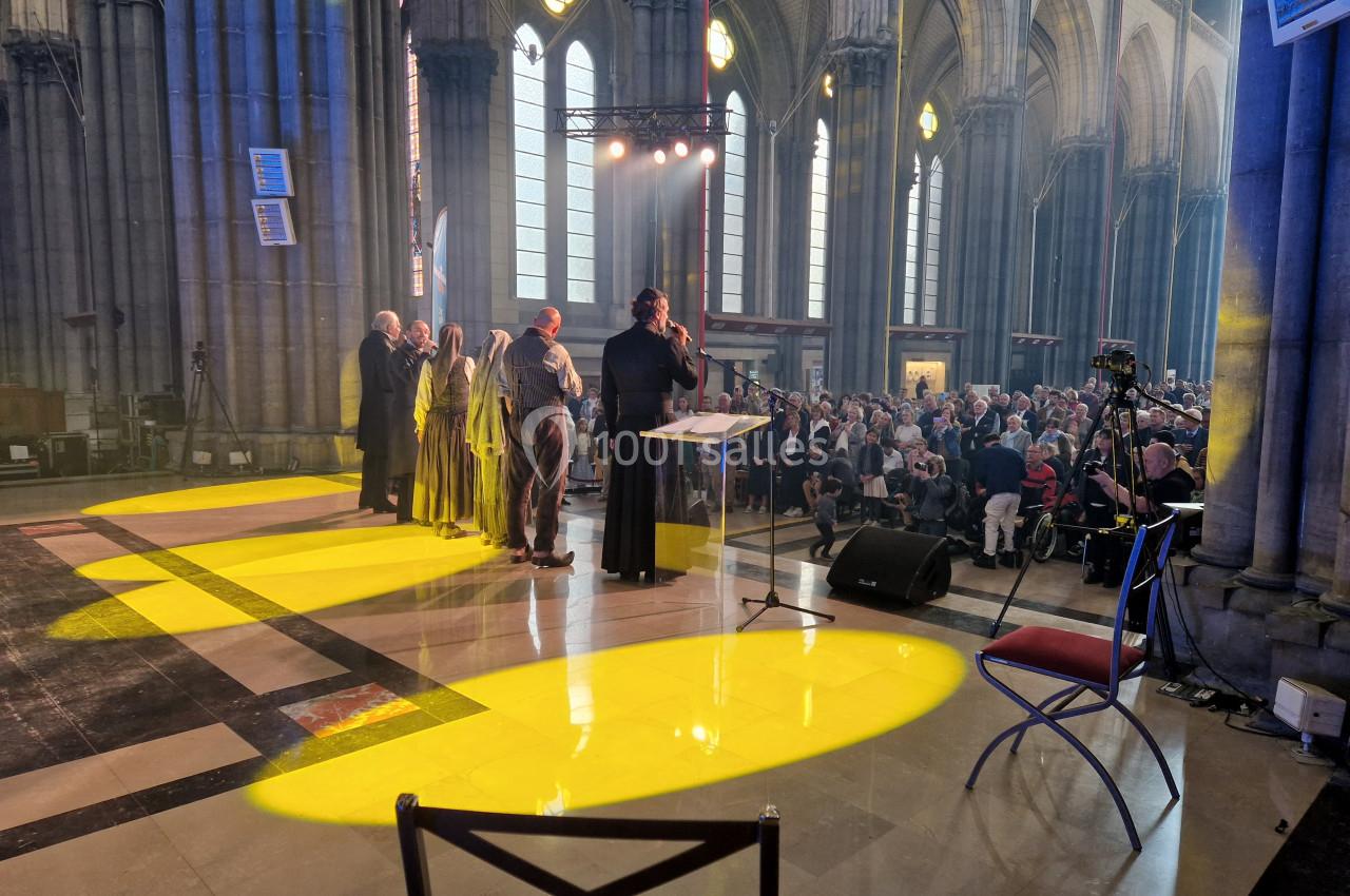 Un groupe de personnes sur scène dans une cathédrale, face à un public, sous des éclairages jaunes.