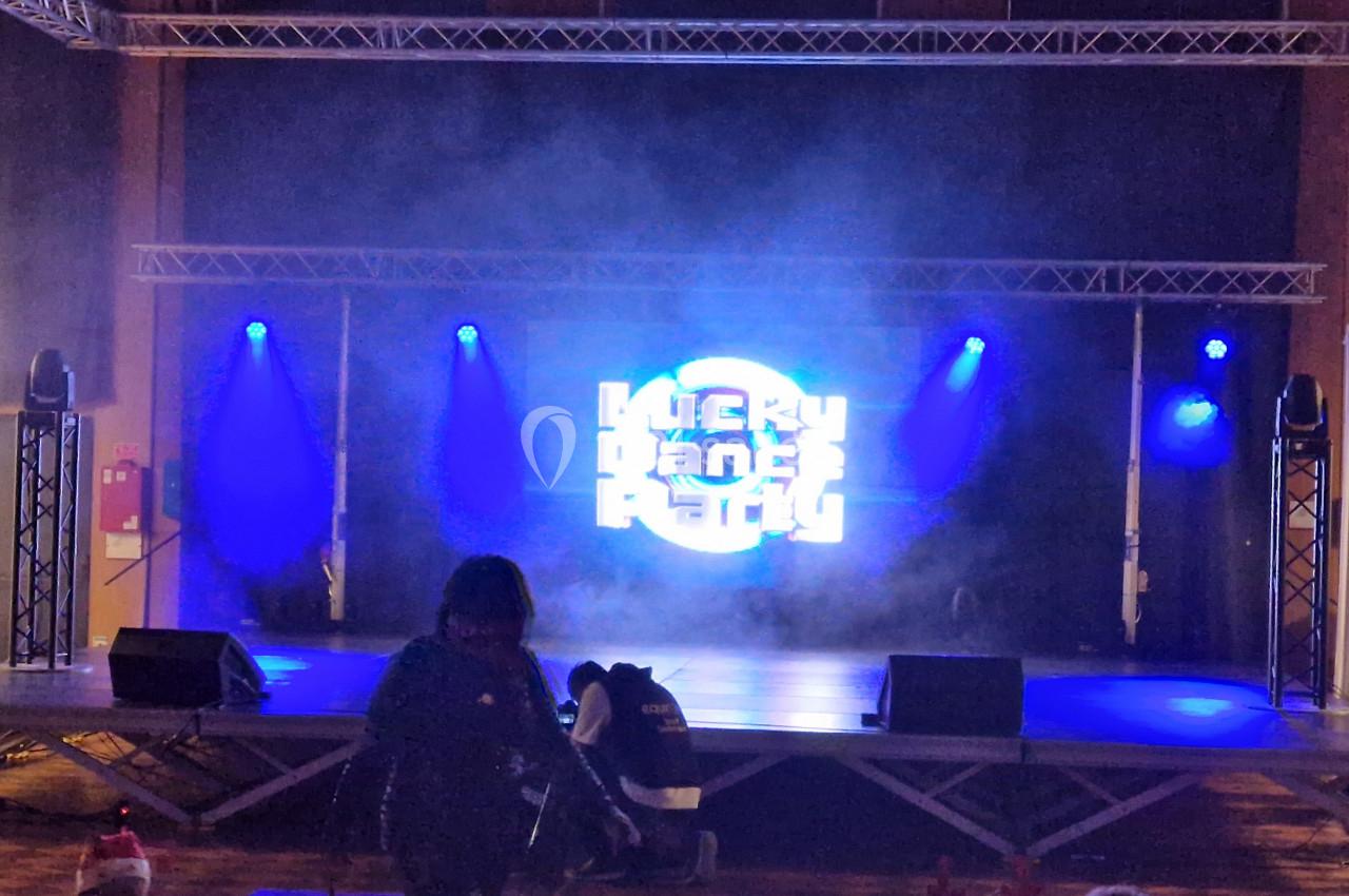 Scène éclairée par des projecteurs bleus avec un écran lumineux affichant un logo, dans une salle sombre.