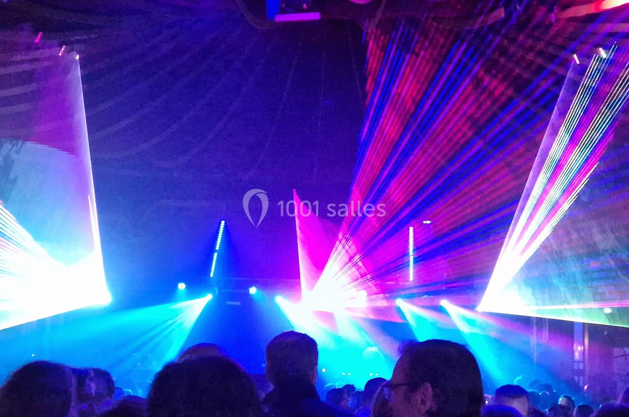 Foule dans une salle sombre illuminée par des faisceaux de lumière colorés et des effets laser.