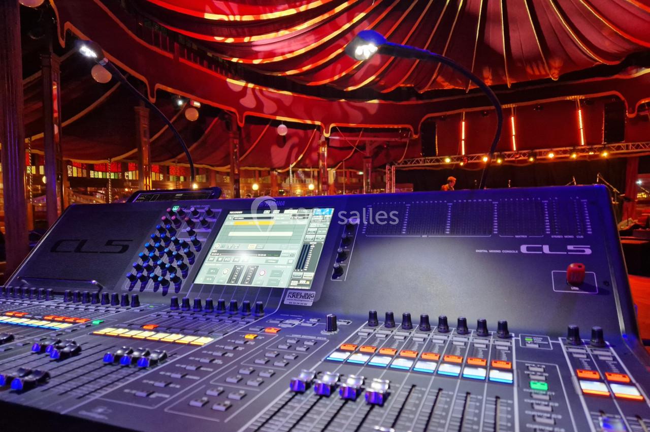 Table de mixage audio numérique dans un chapiteau éclairé par des lumières colorées.