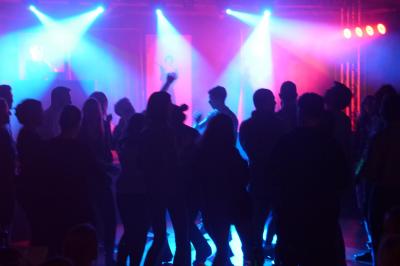 Un bus stationné de nuit devant un bâtiment illuminé, avec des passants en arrière-plan.