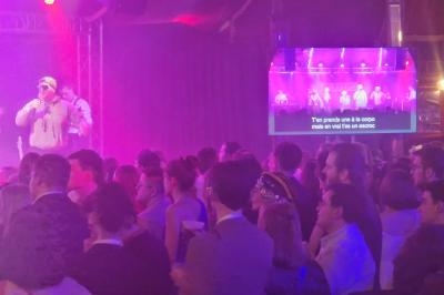 Un bus stationné de nuit devant un bâtiment illuminé, avec des passants en arrière-plan.