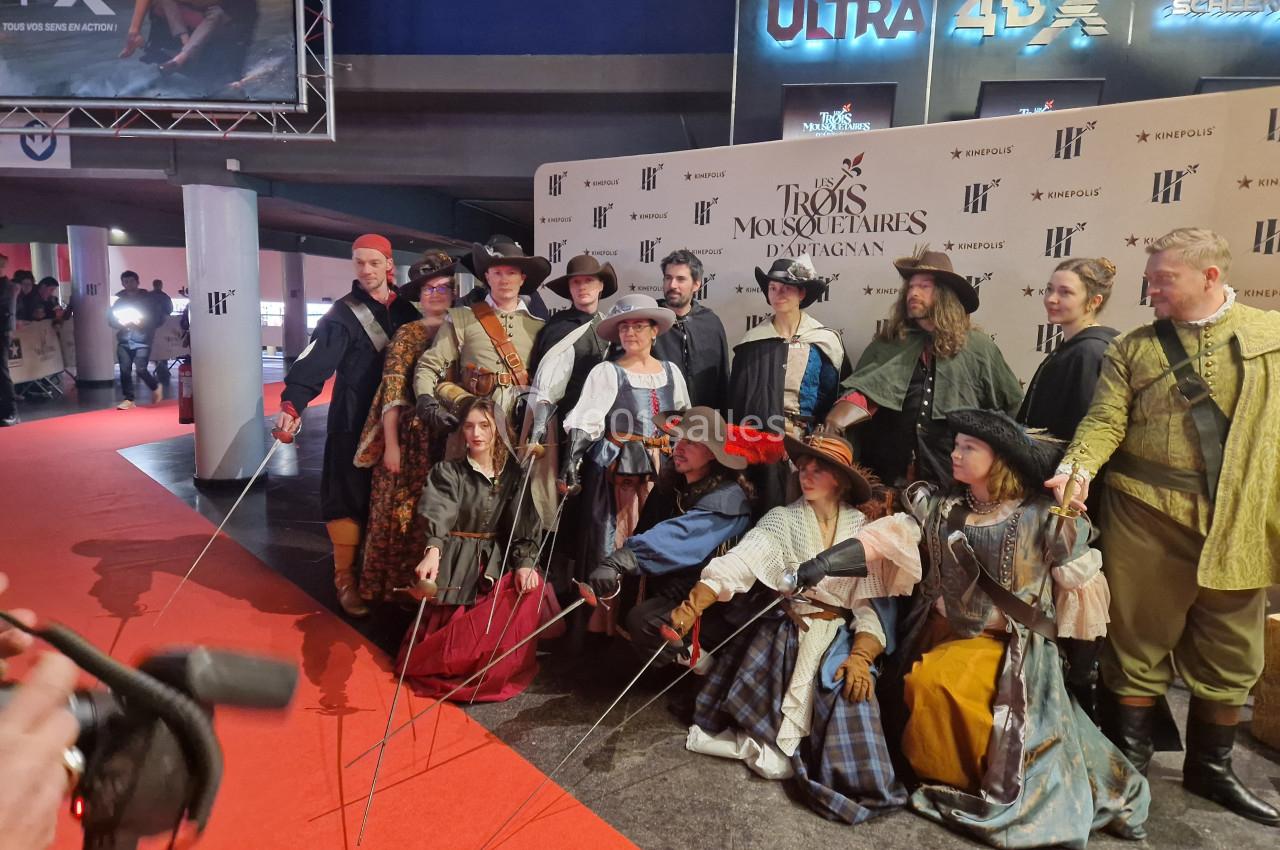 Des personnes en costumes d'époque posent sur un tapis rouge devant un mur avec des logos d'un événement.