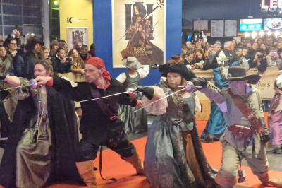 Un bus stationné de nuit devant un bâtiment illuminé, avec des passants en arrière-plan.