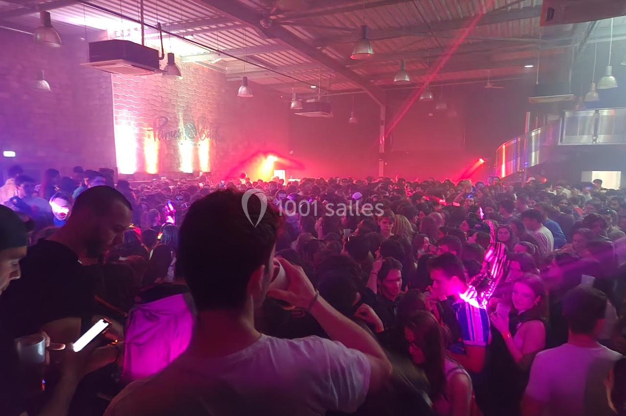 Foule dense dans une salle de concert avec éclairages colorés et ambiance festive.