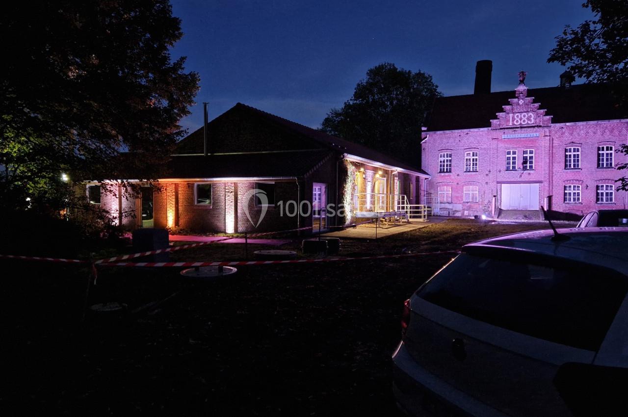 Bâtiments anciens éclairés par des lumières colorées dans un environnement nocturne avec des arbres et des voitures.