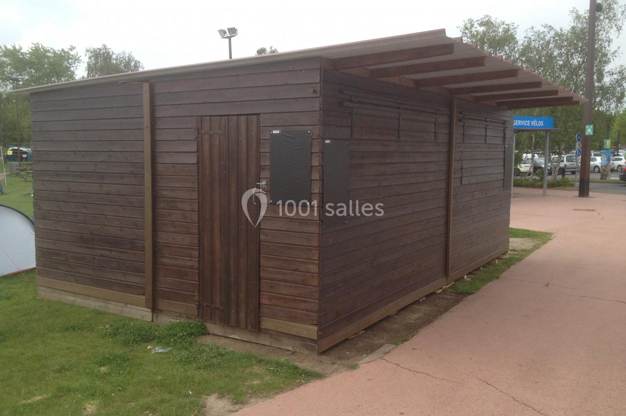 Abri en bois avec porte et toit incliné, situé sur un espace vert près d'une allée pavée.