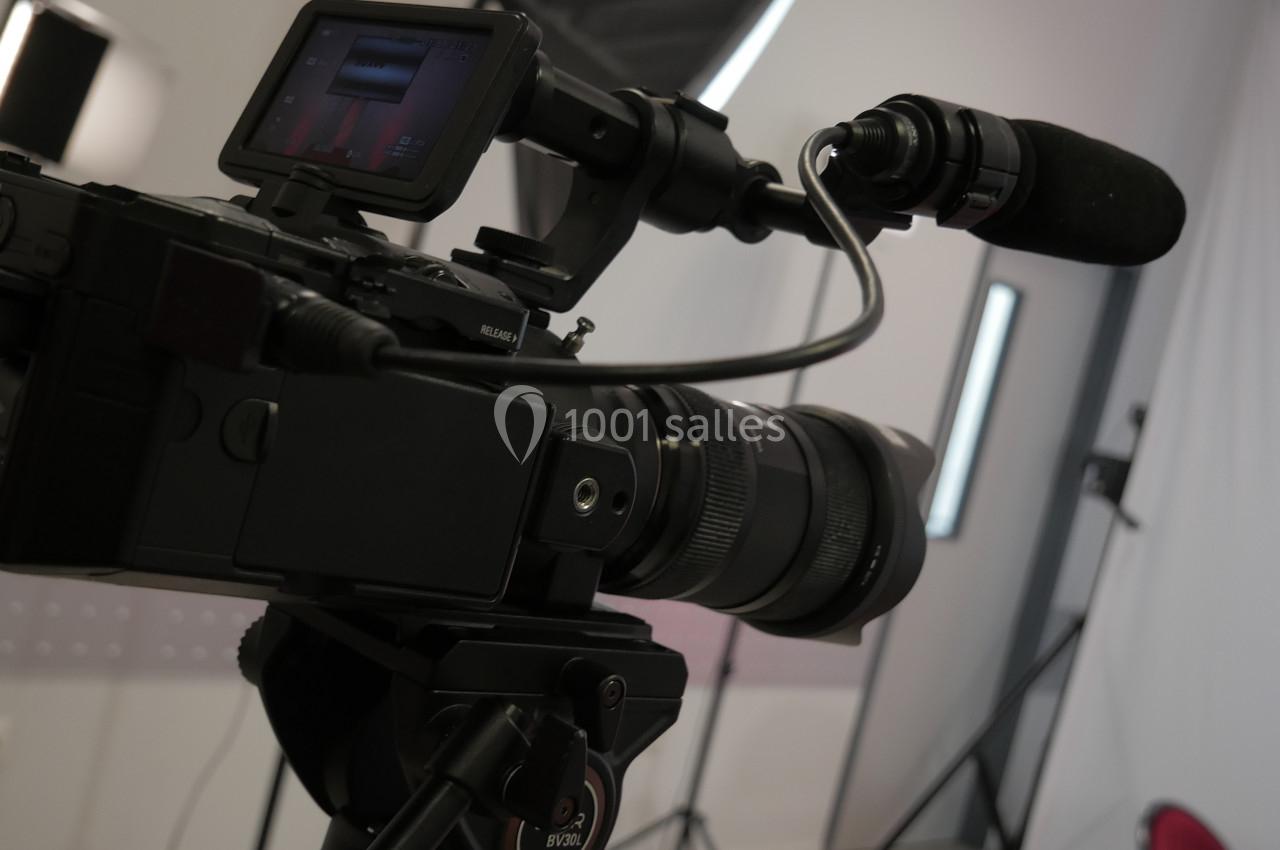 Caméra professionnelle avec micro montée sur trépied dans un studio avec éclairage et fond blanc.