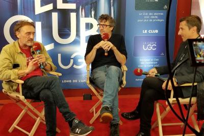 Un bus stationné de nuit devant un bâtiment illuminé, avec des passants en arrière-plan.