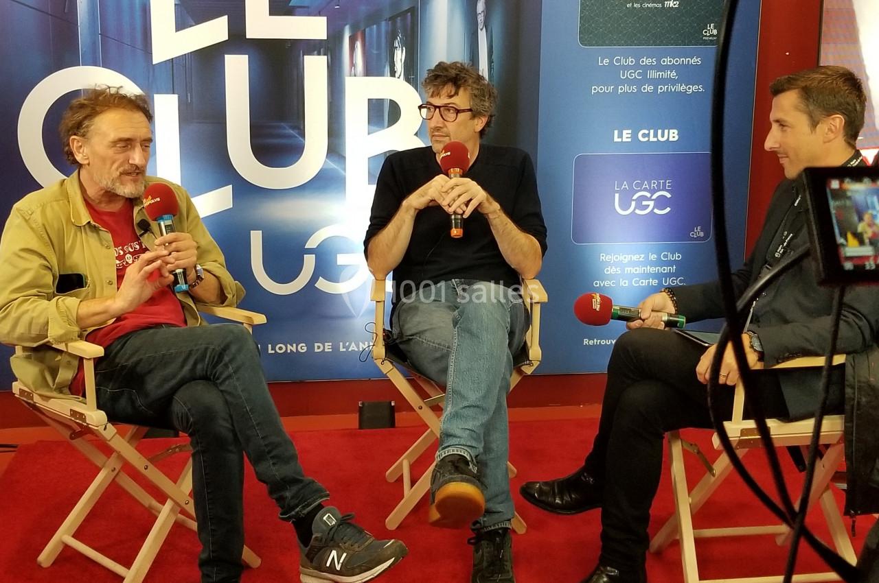 Trois personnes discutent sur des chaises pliantes lors d'une interview filmée dans un espace promotionnel.