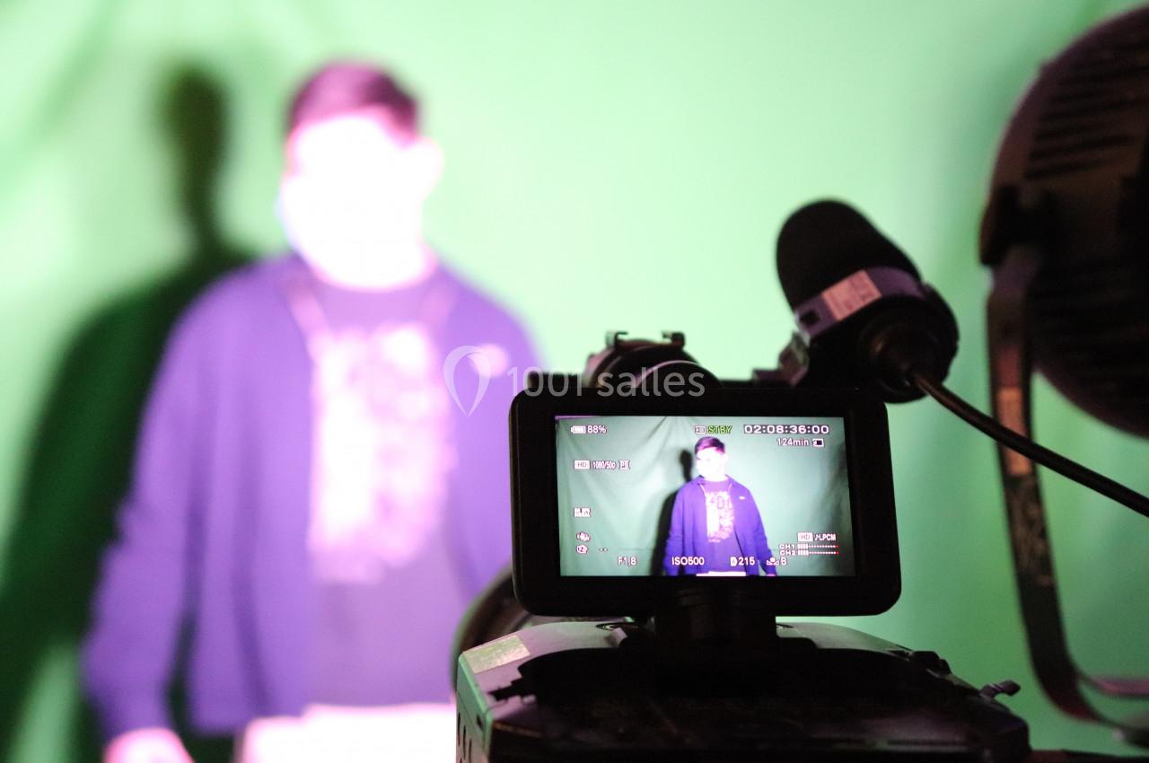 Une caméra filme une personne debout devant un fond vert, visible à travers l'écran de contrôle.