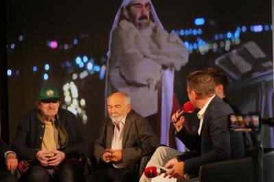 Un bus stationné de nuit devant un bâtiment illuminé, avec des passants en arrière-plan.