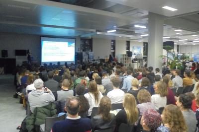Un bus stationné de nuit devant un bâtiment illuminé, avec des passants en arrière-plan.