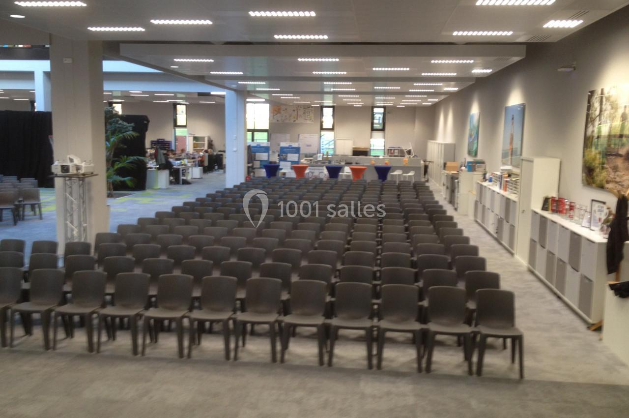Salle de conférence avec des rangées de chaises vides, éclairage artificiel et stands en arrière-plan.