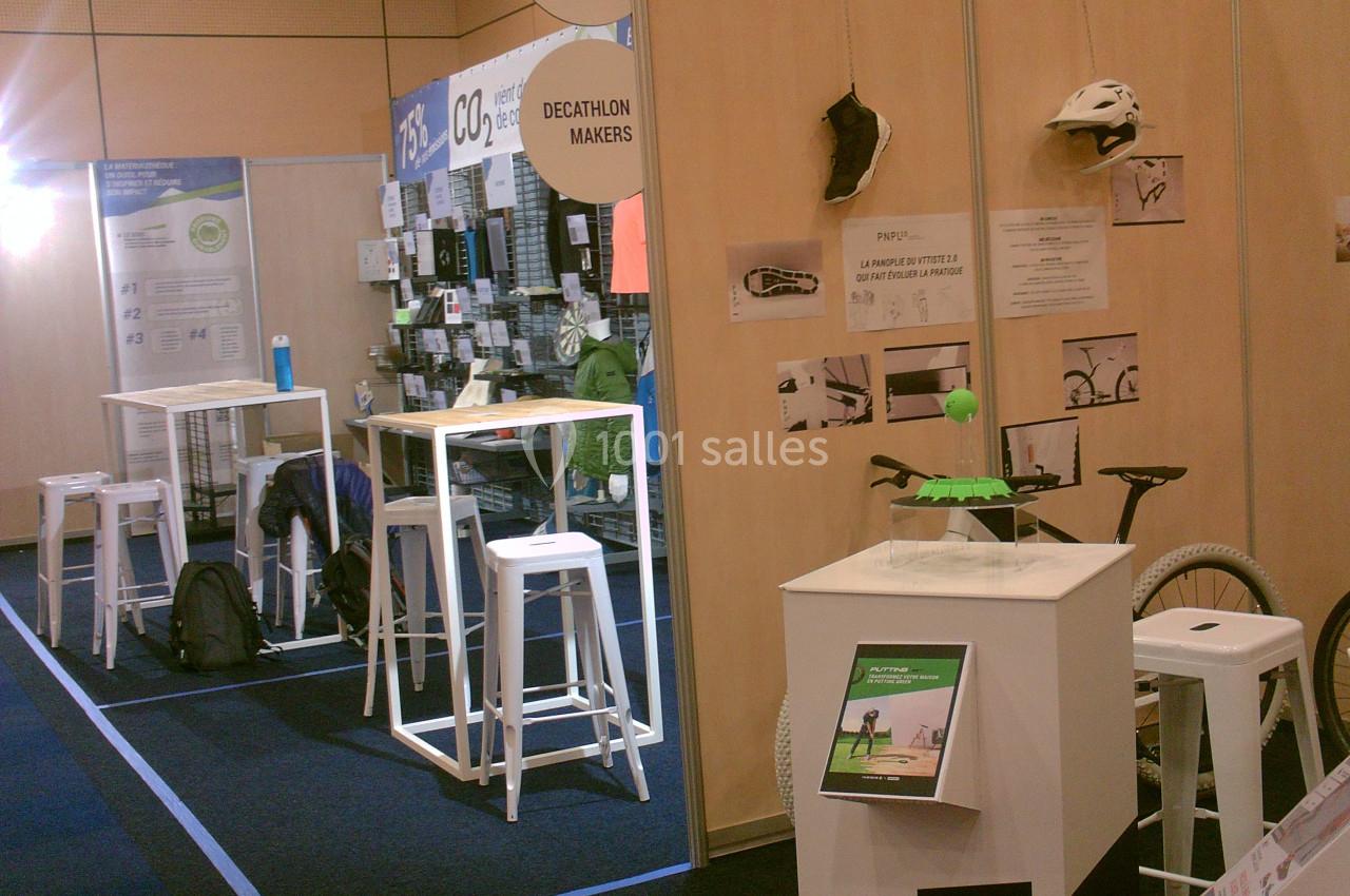 Stand d'exposition avec des présentoirs, tabourets hauts, affiches informatives et accessoires de vélo exposés.