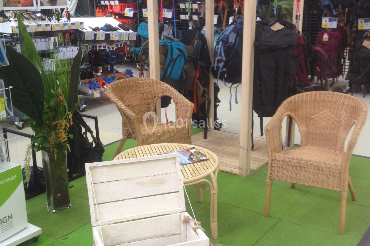 Espace d'exposition en magasin avec mobilier en rotin, plantes décoratives et présentoirs de sacs à dos en arrière-plan.