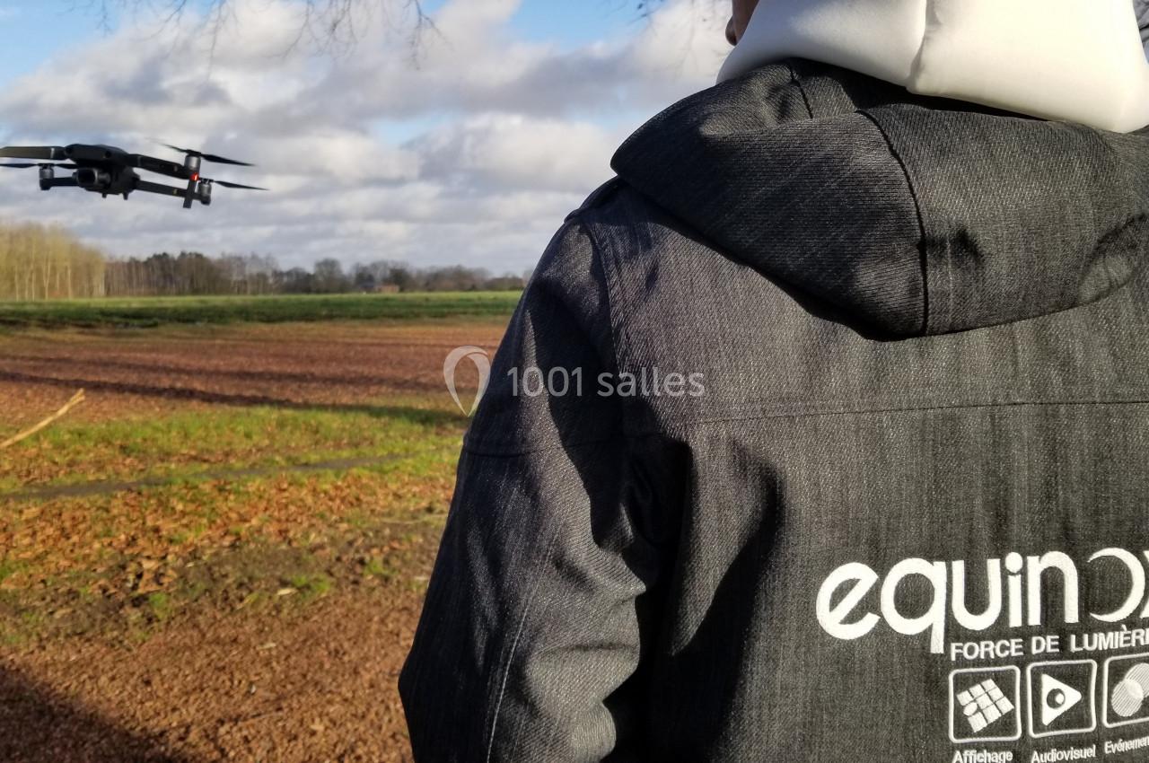 Une personne pilote un drone en plein vol au-dessus d'un champ, par une journée partiellement nuageuse.