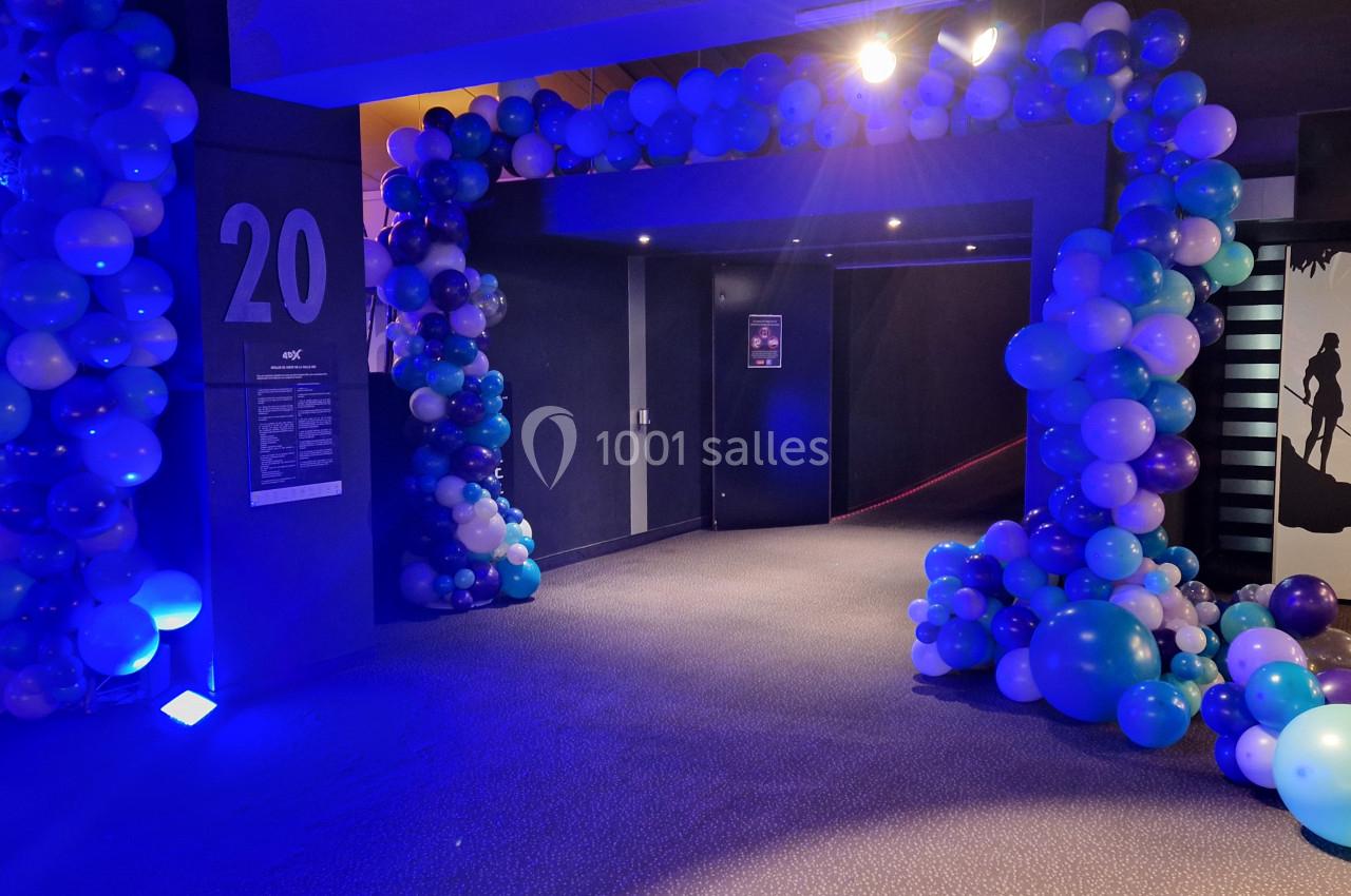 Entrée décorée d'arcs de ballons bleus et violets, éclairée par une lumière tamisée dans un couloir.