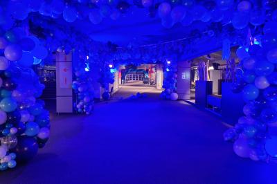 Un bus stationné de nuit devant un bâtiment illuminé, avec des passants en arrière-plan.