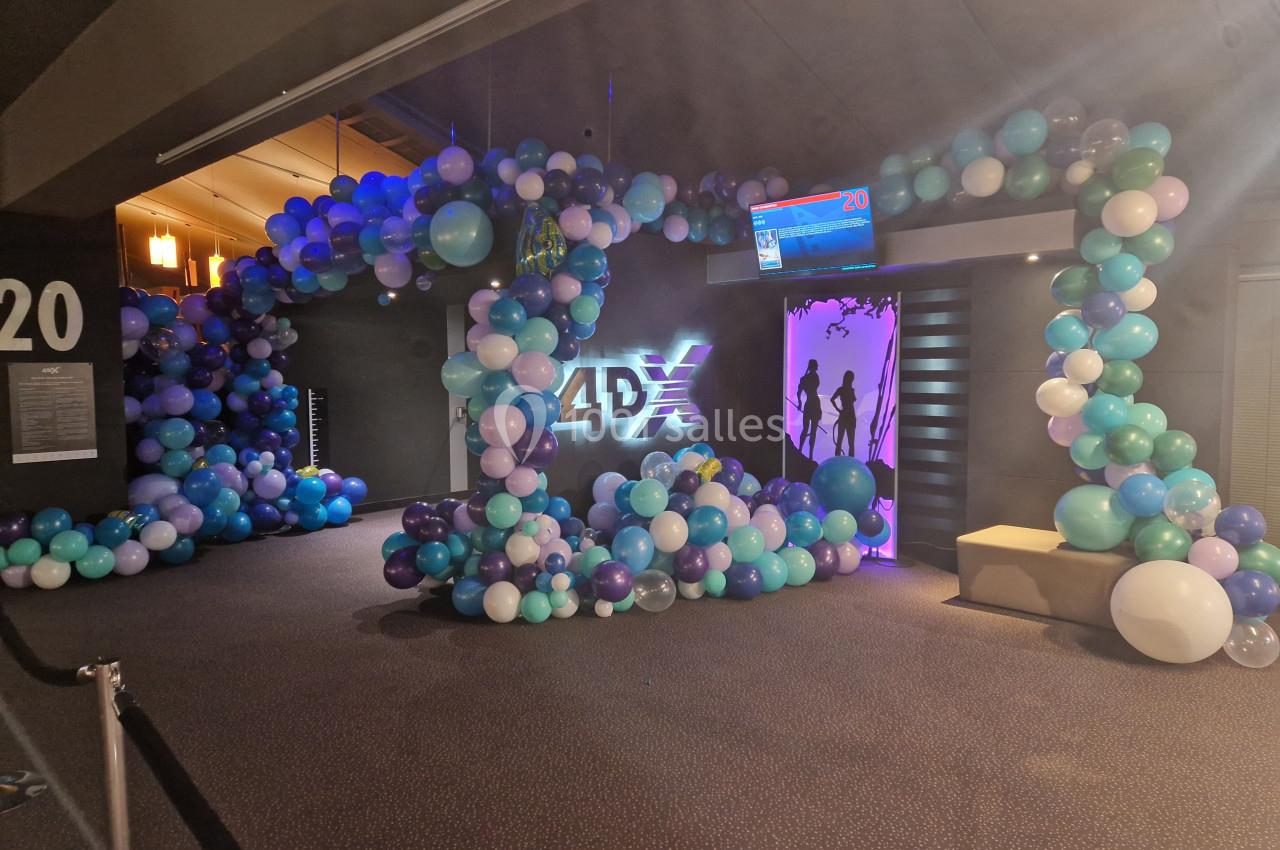 Entrée d'une salle de cinéma 4DX décorée avec des ballons multicolores et un écran d'affichage lumineux.