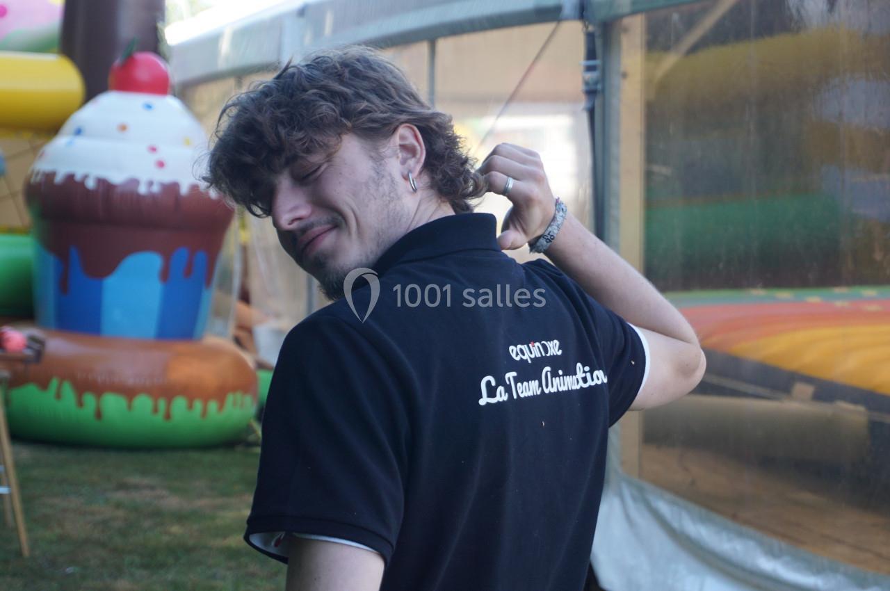 Un homme de dos portant un polo noir avec une inscription, devant des structures gonflables colorées en extérieur.