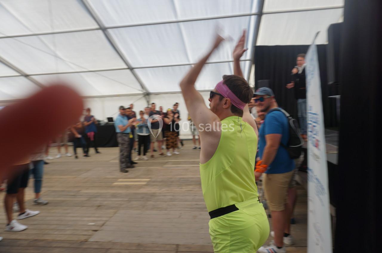 Un homme en tenue sportive jaune danse sous une tente devant un public debout.