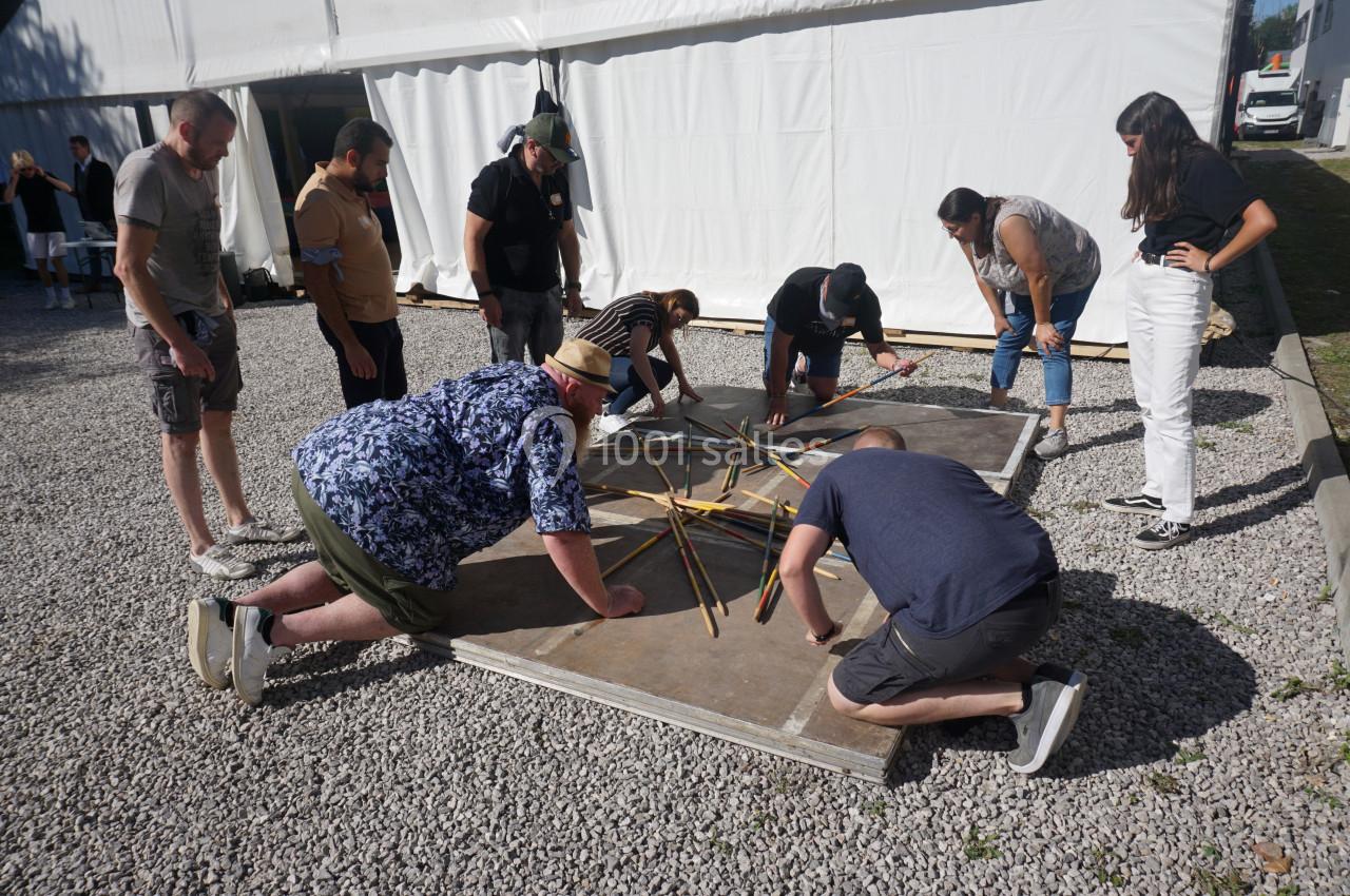 Des personnes participent à une activité collaborative en extérieur, manipulant de longs bâtons disposés en étoile.
