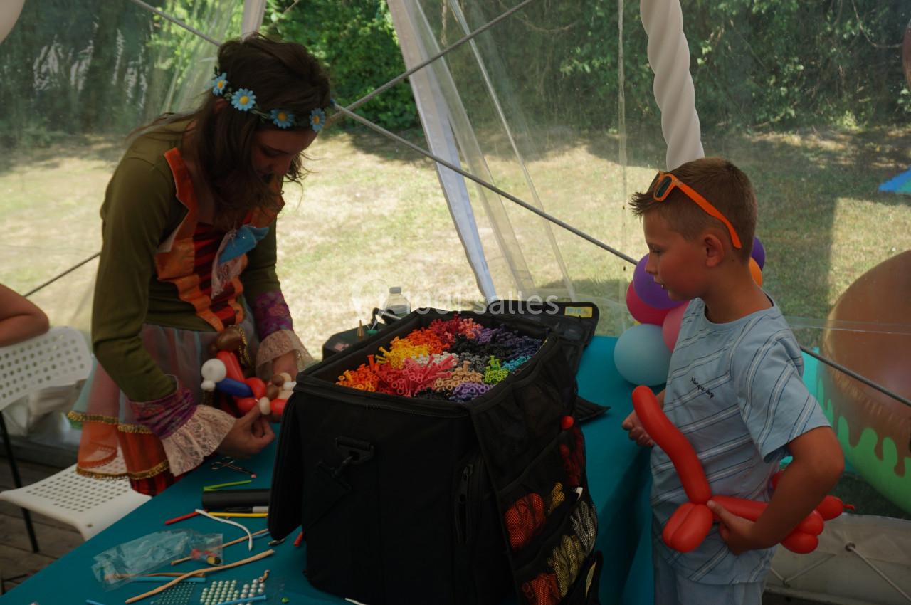 Une femme crée des sculptures en ballons devant un enfant dans une tente lors d'un événement en plein air.