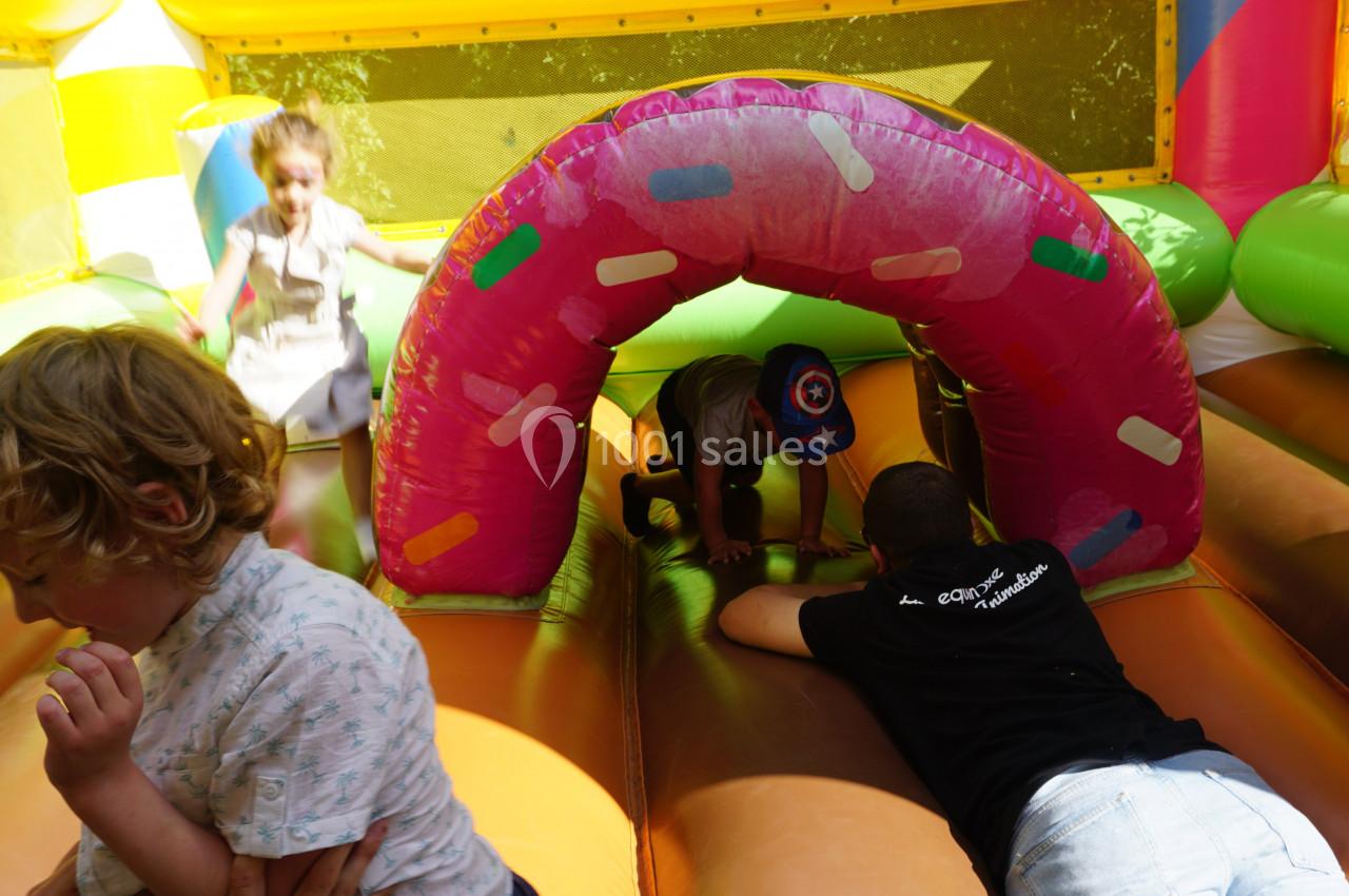Des enfants et un adulte jouent dans une structure gonflable colorée avec un tunnel décoré de motifs.