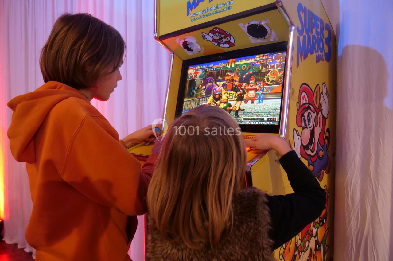 Deux enfants jouent à un jeu vidéo rétro sur une borne d'arcade jaune décorée de personnages de Mario.