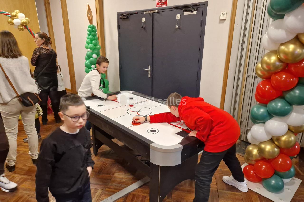 Deux enfants jouent à un jeu de hockey sur table dans une salle décorée de ballons colorés.