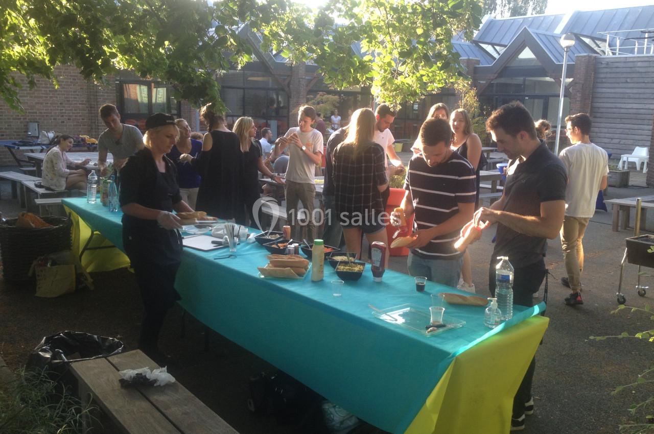 Personnes réunies autour de tables en extérieur, préparant et partageant de la nourriture dans une ambiance conviviale.