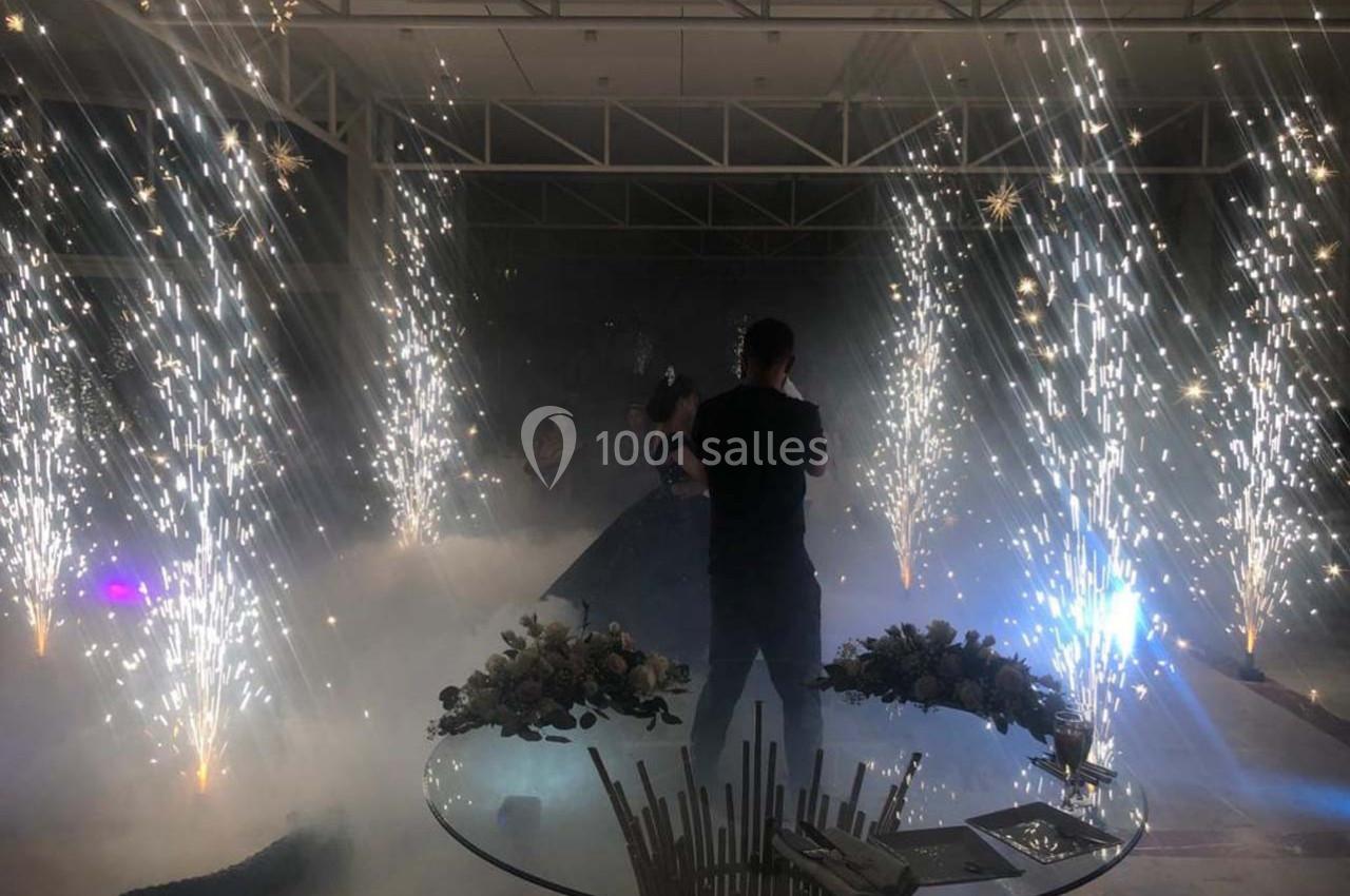 Un couple danse au centre d'une salle illuminée par des feux d'artifice intérieurs et entourée de fumée légère.