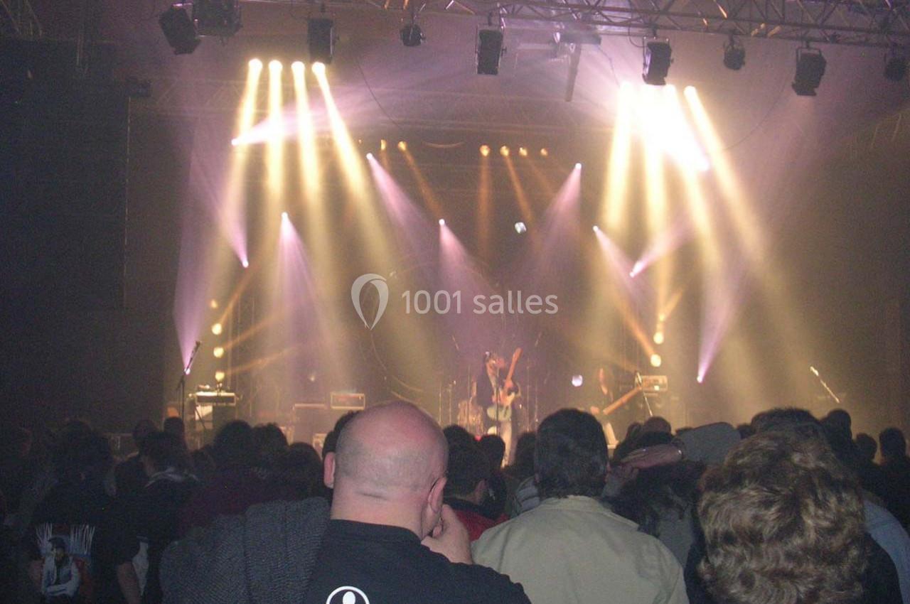 Foule assistant à un concert dans une salle sombre, éclairée par des projecteurs colorés sur la scène.