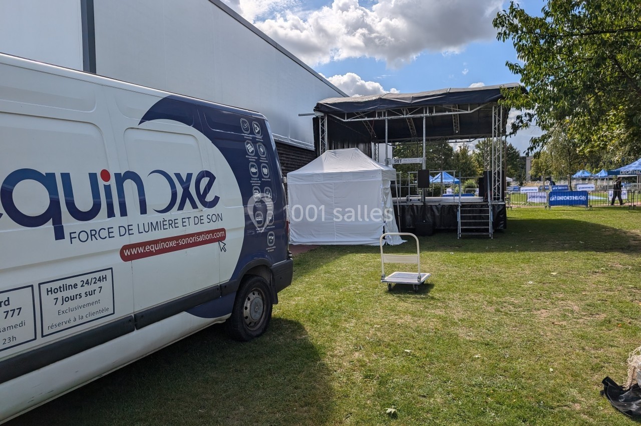 Camion de prestation technique stationné près d'une scène extérieure en montage, sur une pelouse par temps ensoleillé.