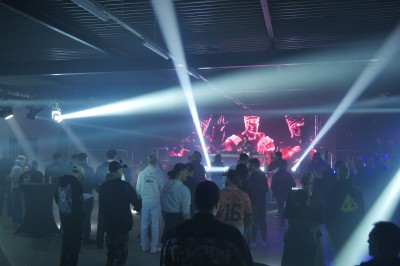 Miniature Equinoxe #161 Un bus stationné de nuit devant un bâtiment illuminé, avec des passants en arrière-plan.