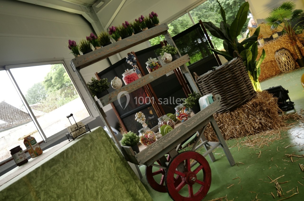 Chariot en bois décoré de bonbonnières et plantes, entouré de bottes de paille et de végétation dans un espace intérieur…