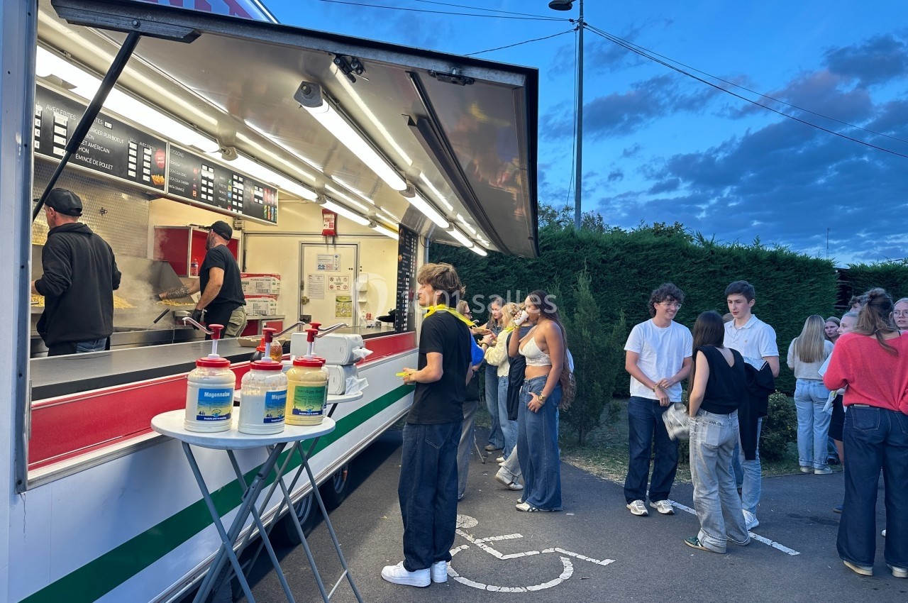 Un food truck ouvert en soirée avec des clients attendant leur commande devant le comptoir éclairé.
