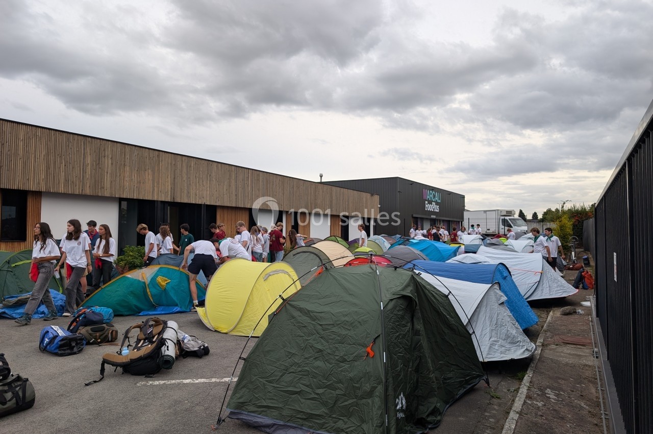 Des tentes installées sur un parking devant un bâtiment, avec des groupes de personnes rassemblées autour.