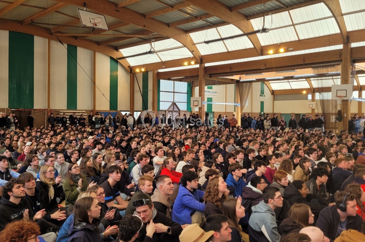 Un large groupe de personnes assises dans un gymnase, assistant à un événement ou une présentation.