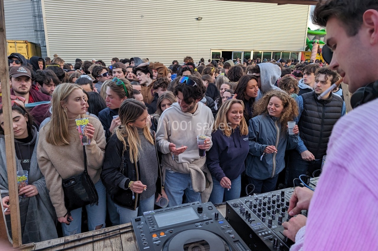 Un DJ mixe en plein air devant une foule de jeunes adultes rassemblés pour un événement festif.