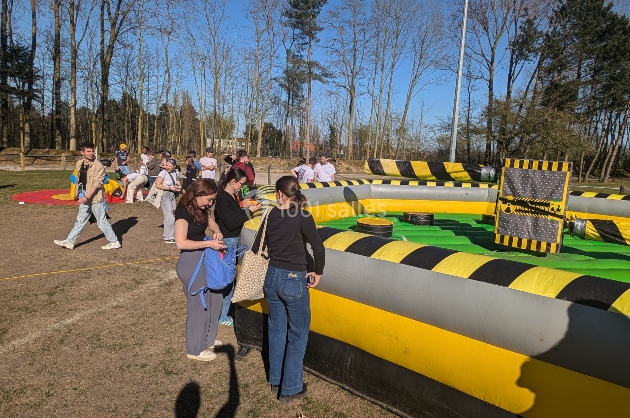 Des personnes participent à une activité de plein air autour d'une structure gonflable jaune et noire dans un parc.